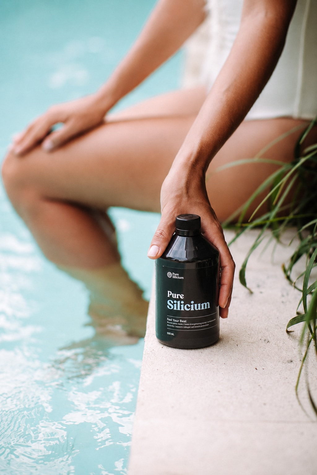 A hand sets a Pure Silicium bottle on a pool ledge