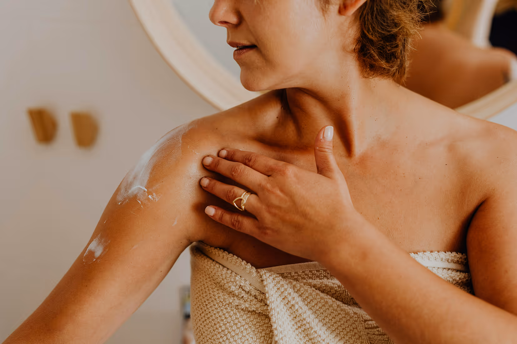 A woman applying Pure Silicium to her shoulder in warm bathroom light